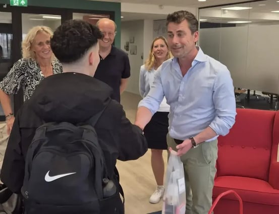 Yousef krijgt een hand van Eric tijdens een ontmoeting op kantoor, terwijl drie andere mensen toekijken.