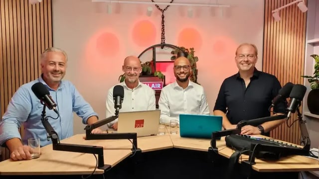 Patrick, Hugo-Jan, Narada en Chris poseren samen in een podcaststudio achter microfoons en laptops.